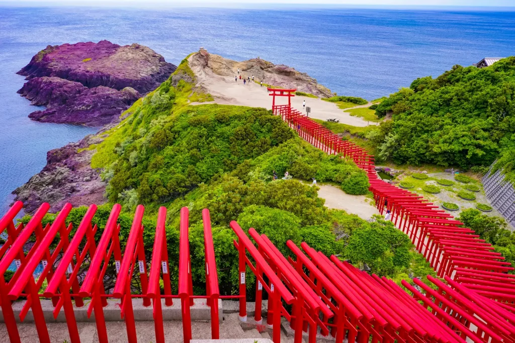 山口県の元乃隅神社。朱色の鳥居が連なり、海に向かって伸びる絶景。駐車場やアクセス情報も含まれるイメージ。
